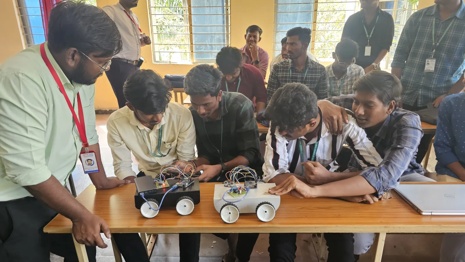 Students and a trainer examining wheeled robotics projects during a practical workshop